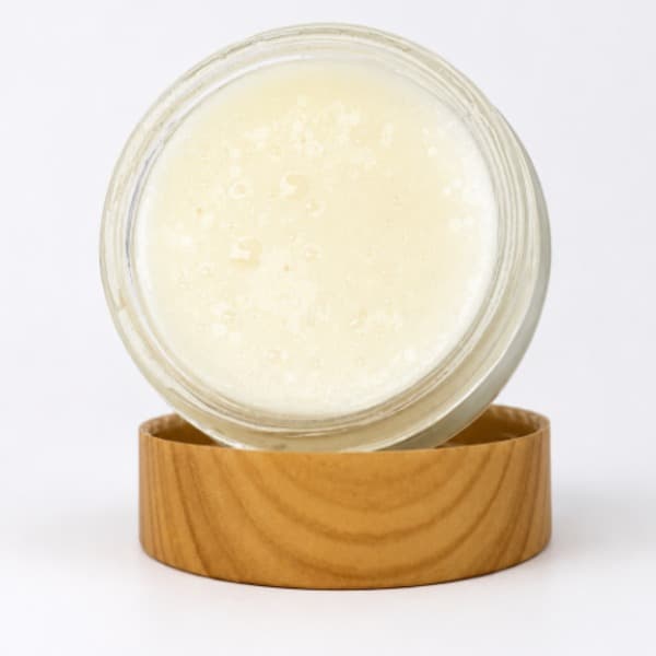 An open frosted jar sitting in a wood grain lid containing frankincense resin and castor oil tallow balm