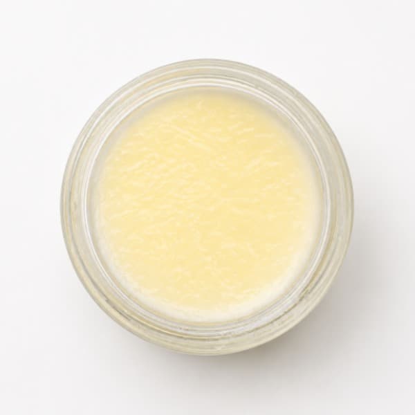 An open jar of a light yellow tallow balm
